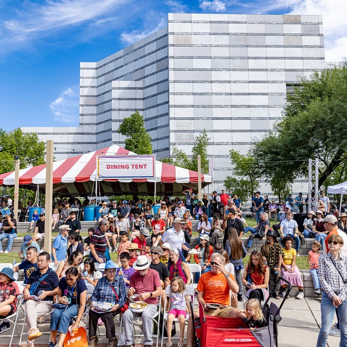 A colorful crowd gathers on Jacome Plaza in front of a dining tent waiting for a show to begin.