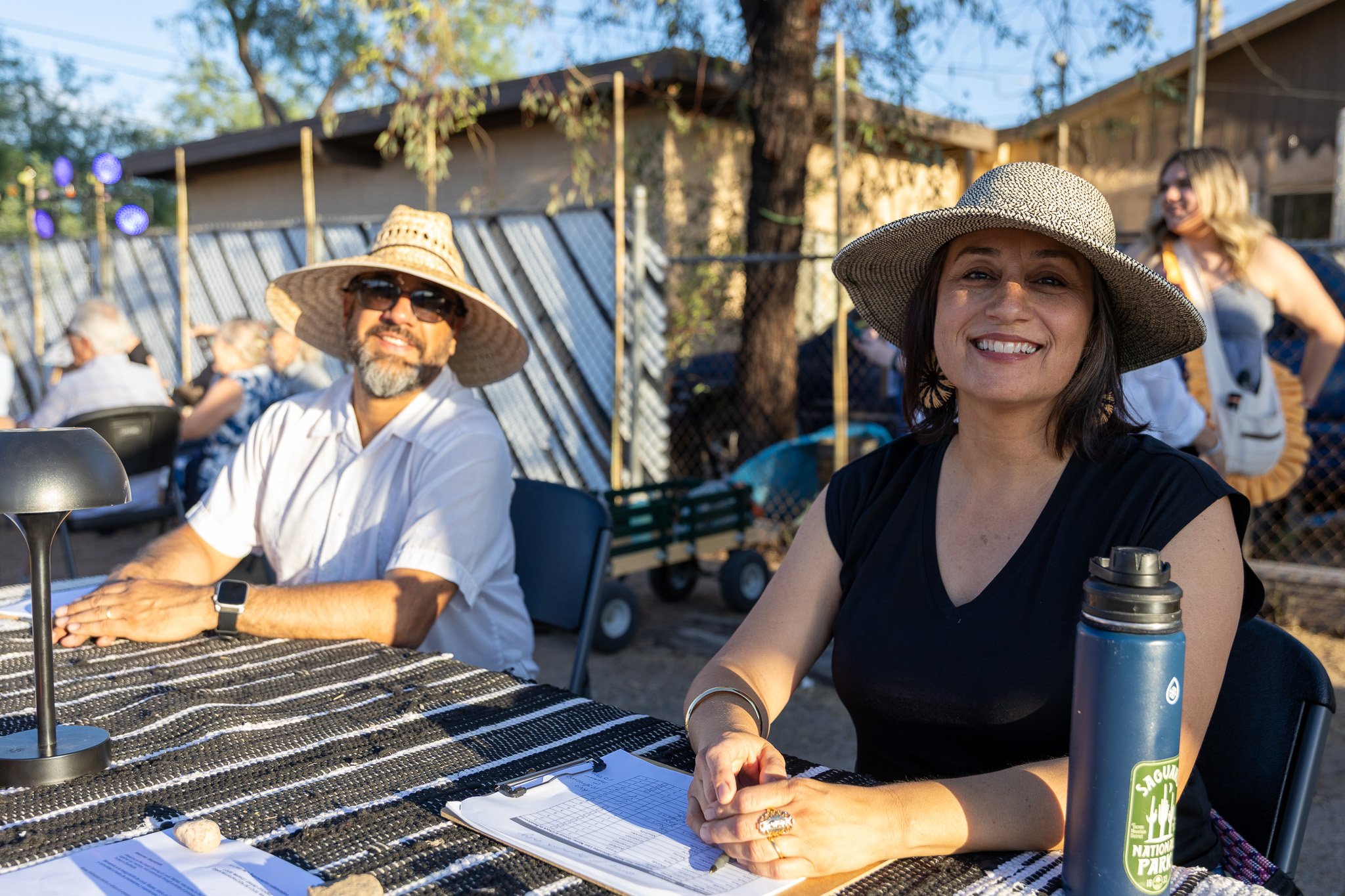 Two smiling people in sun hats sit at a check in table.