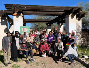 A gathering of Black people of all ages in the garden with a white structure in the background.