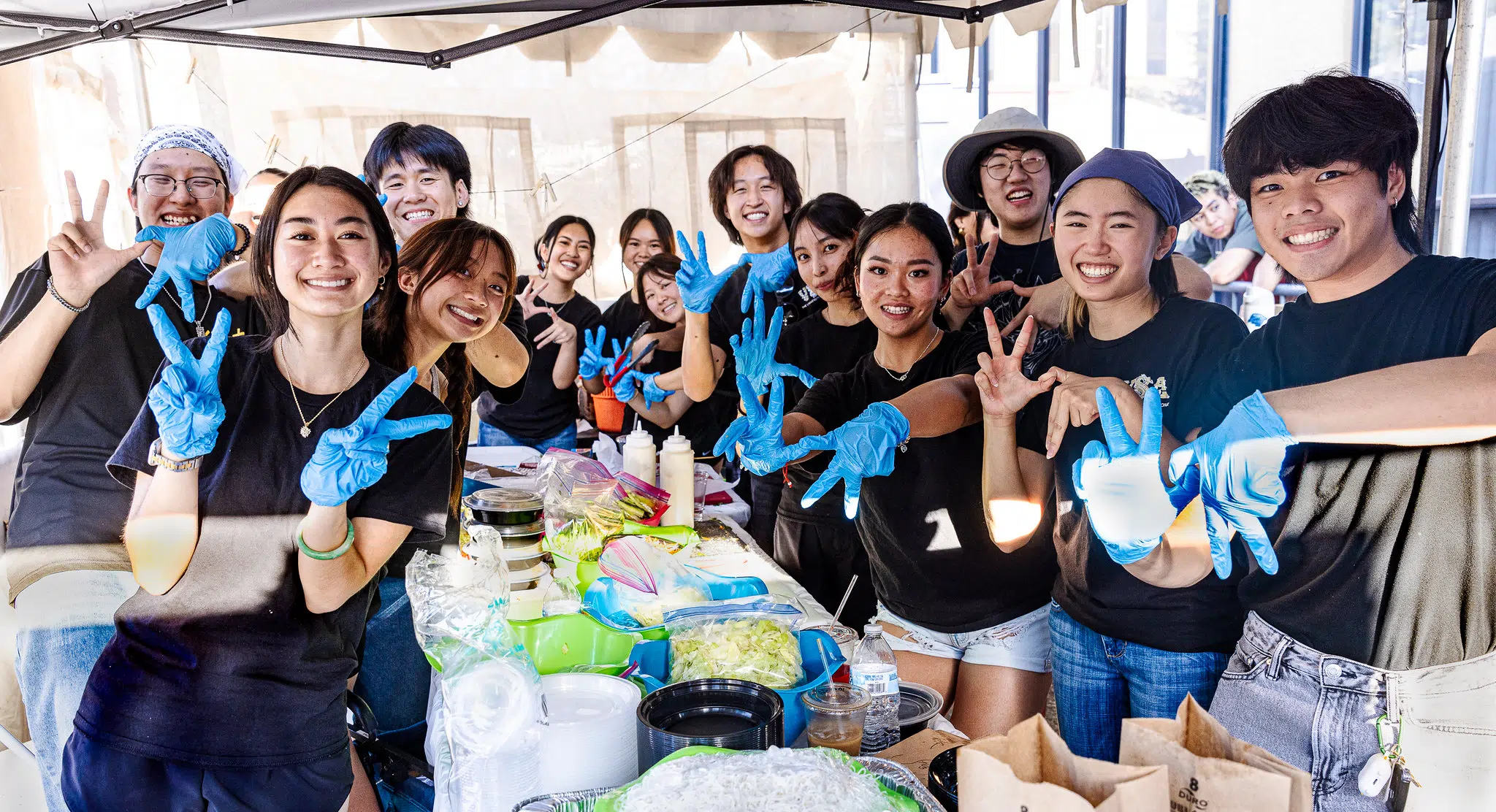 Smiling Vietnamese students wearing blue latex gloves making a "V" and "A" with their hands.