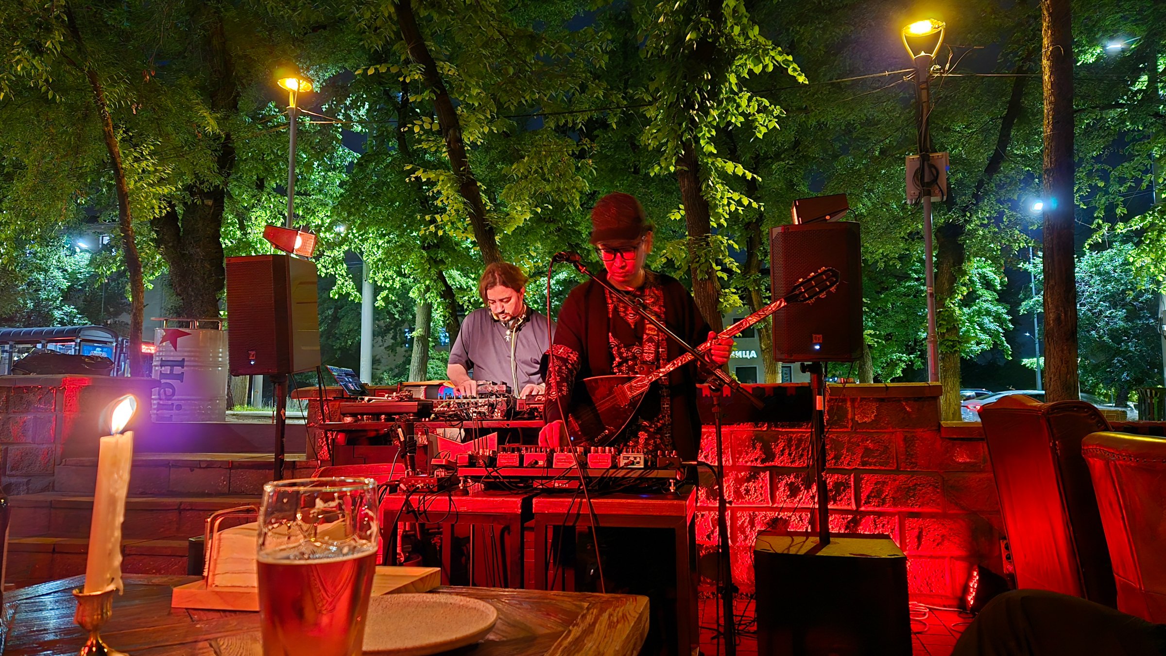 A person playing guitar with several pedals and a DJ behind them.